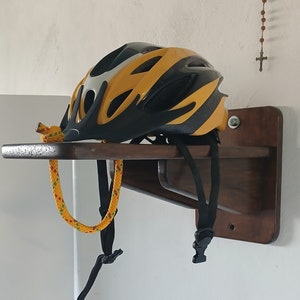 Pode incluir: Um capacete de bicicleta amarelo e preto com uma faixa branca pendurado em uma prateleira de madeira com uma corda amarela e verde.