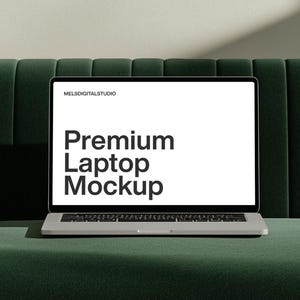 May include: A silver laptop computer with a blank screen is sitting on a dark green velvet sofa. The screen displays the text "Premium Laptop Mockup".