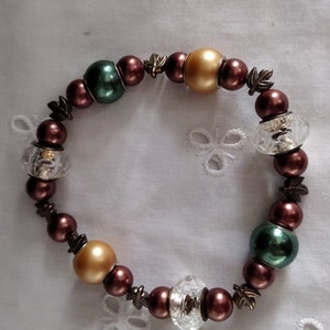 May include: A brown, green, and gold beaded bracelet with clear crystal accents. The bracelet is made of round beads and has a simple design.