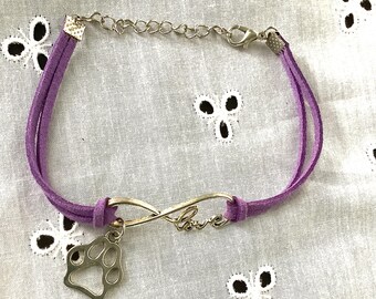 May include: Purple suede bracelet with an infinity symbol charm and a paw print charm. The infinity symbol charm has the word "love" inscribed on it.