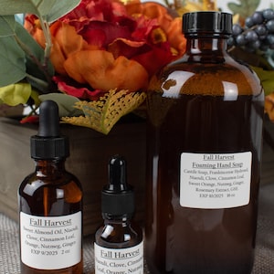 Könnte beinhalten: Drei bernsteinfarbene Glasflaschen mit Tropfern und Etiketten. Die Flaschen enthalten ätherische Öle und Handseife mit Herbst-Duftnoten. Die Etiketten listen die Inhaltsstoffe und Verfallsdaten auf. Die Flaschen sind auf einer braunen Jutestoff-Oberfläche angeordnet.