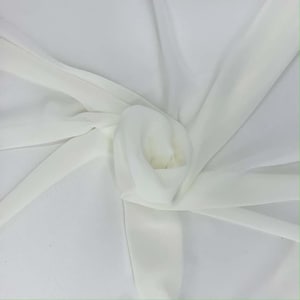 May include: A close-up of a white fabric with a soft, flowing texture. The fabric is gathered and folded, creating a layered effect. The material appears to be lightweight and semi-transparent, with subtle highlights and shadows.