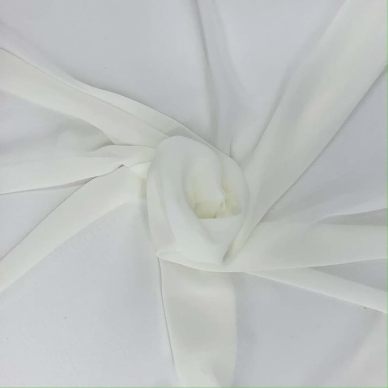 May include: A close-up of a white fabric with a soft, flowing texture. The fabric is gathered and folded, creating a layered effect. The material appears to be lightweight and semi-transparent, with subtle highlights and shadows.