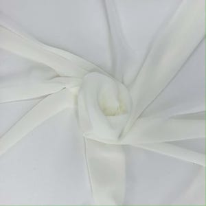 May include: A close-up of a white fabric with a soft, flowing texture. The fabric is gathered and folded, creating a layered effect. The material appears to be lightweight and semi-transparent, with subtle highlights and shadows.