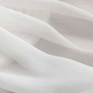 May include: Close-up of white fabric with soft folds and a translucent appearance. The fabric has a delicate texture and a subtle sheen, creating a sense of movement and flow. The image highlights the fabric's lightness and airy quality.