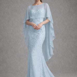 K&ouml;nnte beinhalten: Ein hellblaues, bodenlanges Kleid mit Meerjungfrau-Silhouette. Das Kleid hat zarte Blumenstickereien und einen transparenten Umhang. Das Kleid eignet sich f&uuml;r formelle Anl&auml;sse wie Hochzeiten oder Galas.