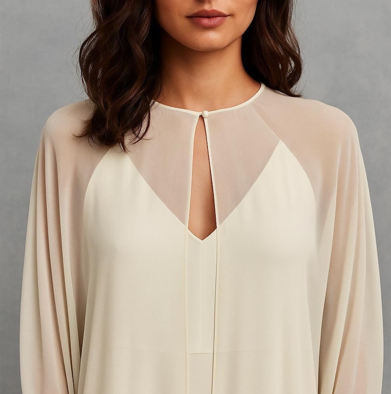 May include: Cream-colored dress with sheer, light beige overlay. The dress features a V-neckline and a keyhole detail at the neckline, fastened with a small button. The sleeves are long and flowing, creating an elegant silhouette.