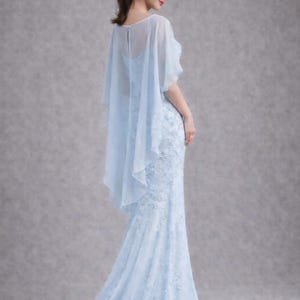 K&ouml;nnte beinhalten: Ein hellblaues, bodenlanges Kleid mit aufwendigen Spitzendetails. Das Kleid hat eine figurbetonte Silhouette, die sich am Saum ausstellt. Ein durchsichtiges, flie&szlig;endes Capelet bedeckt die Schultern und verleiht einen eleganten Touch. Das Kleid ist f&uuml;r formelle Anl&auml;sse geeignet.