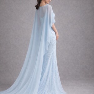 K&ouml;nnte beinhalten: Ein hellblaues, bodenlanges Kleid mit einem flie&szlig;enden Umhang. Das Kleid hat aufwendige Spitzendetails und eine figurbetonte Silhouette. Der Umhang f&auml;llt elegant von den Schultern und erzeugt einen weichen, &auml;therischen Look. Der Stoff wirkt leicht und luftig.