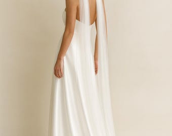 May include: A white satin wedding dress with a flowing skirt and a halter-style bodice. The dress features sheer, flowing fabric that drapes from the shoulders. The bride's hair is styled in an updo.