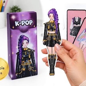 May include: A K-Pop themed paper doll set. The box, with "K-POP" on it, features a purple-haired character in a black outfit with gold accents. Includes "8 Printable Pages". Additional outfits are shown on pink cards.