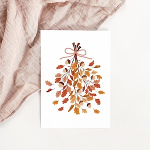 May include: A white card featuring a fall-themed illustration. The artwork depicts a bundle of oak leaves and acorns in shades of orange, brown, and yellow, tied with a pink bow. The card is set against a soft, pink fabric background.