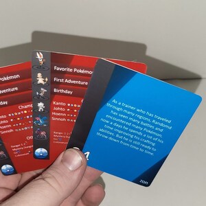 Puede incluir: Tres cartas rojas y azules con texto sobre juegos de Pokemon. El texto en la tarjeta azul dice: "Como entrenador que ha viajado por muchas regiones, Randomd ha visto muchas batallas y se ha encontrado con muchos Pokemon, ahora pasa mucho tiempo mejorando su artesan&iacute;a. Pero todav&iacute;a est&aacute; listo para luchar de vez en cuando."