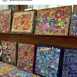 Puede incluir: Una colecci&oacute;n de obras de arte coloridas y estampadas en exhibici&oacute;n. La obra de arte presenta dise&ntilde;os intrincados con tonos vibrantes de rojo, amarillo, azul y verde. Las piezas parecen estar enmarcadas y est&aacute;n dispuestas en una estanter&iacute;a de madera.