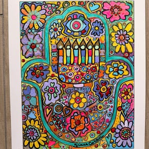May include: A colorful art print featuring a hamsa hand design filled with floral patterns, a central menorah, and eye motifs. The word SHALOM is written vertically on both sides of the menorah. The artist signature grace cohen is visible.