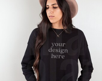 May include: A black cropped sweatshirt with long sleeves and the text "your design here" printed on the front. The model is wearing blue jeans and a brown fedora.