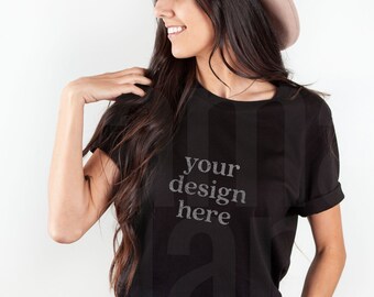 May include: A woman wearing a black t-shirt with the text "your design here" printed on it. She is also wearing a brown fedora hat and blue jeans.