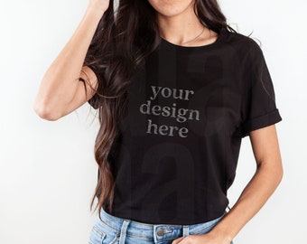 Puede incluir: Camiseta negra con mangas enrolladas y el texto "your design here" en una fuente descolorida. La camiseta se combina con vaqueros de mezclilla azul claro. La persona lleva un anillo.