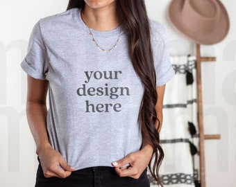 Può includere: Una maglietta grigia con il testo "your design here" stampato sul davanti. La maglietta è indossata da una persona con i capelli lunghi e castani.