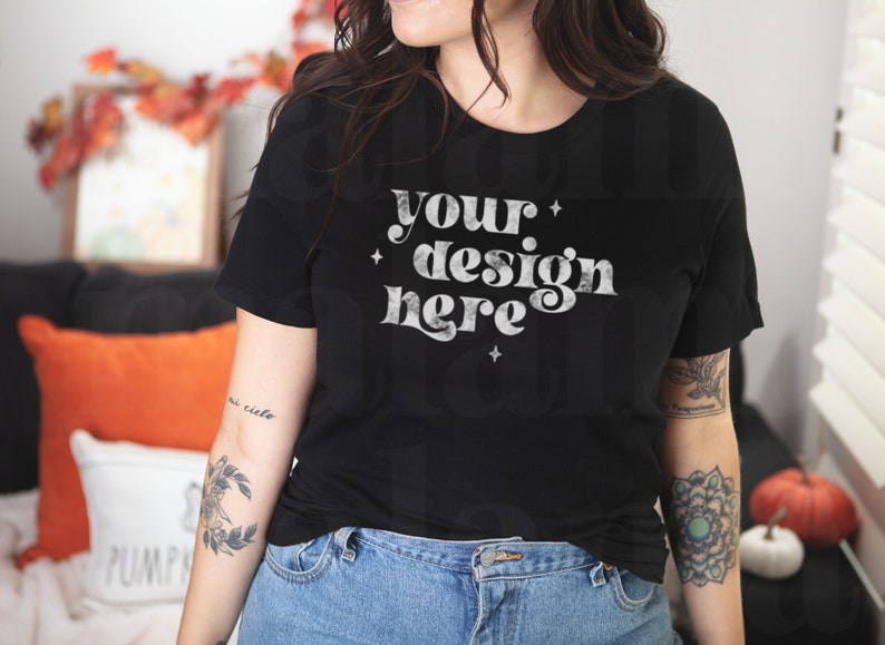 May include: A black t-shirt with the text "your design here" in white with a distressed look. The shirt has a crew neck and short sleeves. The model is wearing blue jeans.