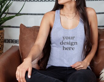 May include: A woman wearing a gray tank top with the text "your design here" printed on the front. She is sitting on a brown leather couch.