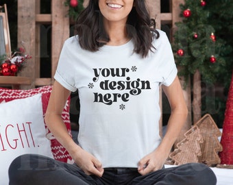 May include: White t-shirt with the text "your design here" in black, with snowflake accents. The shirt is part of a Christmas-themed display, with a red and white pillow, Christmas tree, and other decorations.