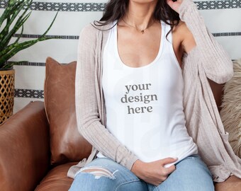 Pode incluir: Uma regata branca com o texto "your design here" é usada com um cardigan bege e jeans azuis. A pessoa está sentada em um sofá de couro marrom. Uma planta de interior em uma cesta tecida é visível ao fundo.