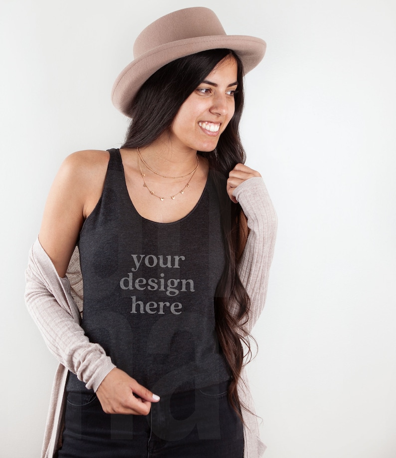 May include: A woman wearing a black tank top with the text "your design here" on it. She is also wearing a brown hat and a beige cardigan.