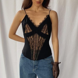 May include: A black satin top with a lace overlay and a plunging neckline. The top is fitted and has a corset-like style. The model is wearing blue jeans.