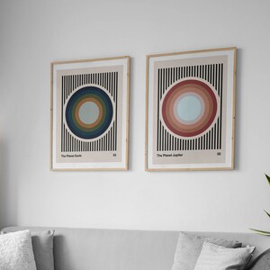 May include: Two framed prints with abstract geometric designs. The print on the left features a blue and green circle with black stripes. The print on the right features a red and pink circle with black stripes. The text on the prints reads "The Planet Earth" and "The Planet Jupiter".