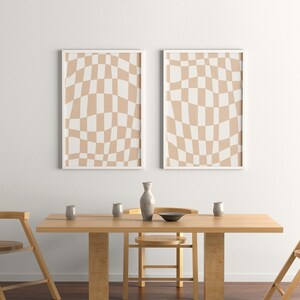May include: Two framed prints with a beige and white checkered pattern hang above a wooden dining table with four chairs. The table is set with a vase, bowls, and glasses.