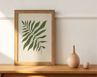 Könnte beinhalten: Ein gerahmter Druck eines grünen Blattdesigns auf weißem Hintergrund. Der Rahmen ist aus Holz und hat eine natürliche Oberfläche. Der Druck hängt an einer weißen Wand über einem Holztisch.