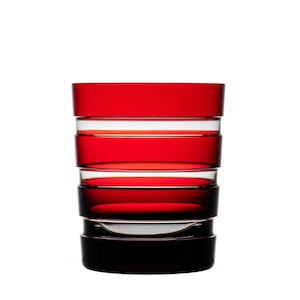 Könnte beinhalten: Ein hohes, rotes Glas mit klaren, horizontalen Bändern. Das Glas hat einen abgerundeten Boden und eine gerade, zylindrische Oberseite.