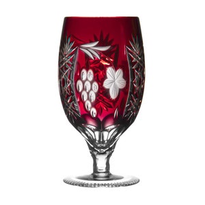 May include: A red crystal wine glass with a cut glass design featuring a grapevine and a cluster of grapes. The glass has a clear stem and base.