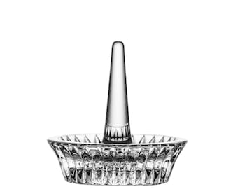 May include: A clear glass ring holder with a decorative, faceted design. The holder has a single, tall, pointed post for holding a ring.