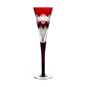 Op de afbeelding: Een hoge, heldere glazen champagnefluit met een rode steel en voet. De fluit heeft een decoratief, geslepen glasontwerp rond de kom.