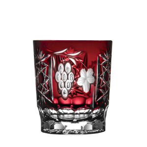 Op de afbeelding: Een rood kristallen glas met een gegraveerd druiven- en bladontwerp aan de zijkant. Het glas heeft een vierkante vorm en een dikke bodem.
