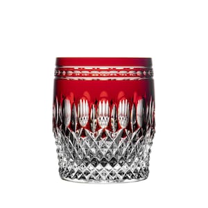May include: A red and clear crystal tumbler with a diamond-cut pattern. The top portion of the glass is solid red, while the bottom half is clear with a detailed, geometric design. This elegant glass is perfect for serving beverages.