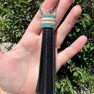 May include: Black leather tassel keychain with a turquoise, white, and orange beaded top. The keychain has a silver ring.