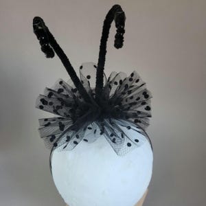 May include: Black headband with a black tulle bow and two black pipe cleaner antennae. The bow has black polka dots.
