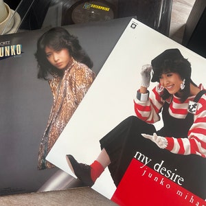 May include: Two vinyl records with album covers featuring a woman in a leopard print coat and a woman in a red and white striped shirt with a black sailor hat. The text on the album covers reads "Secret Junko Mihira" and "My Desire Junko Mihira".