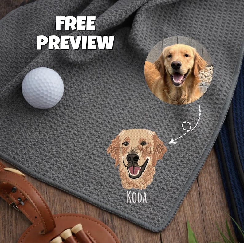 K&ouml;nnte beinhalten: Ein graues Golftuch mit einem gestickten Bild eines Golden Retriever-Hundes und dem Namen "KODA". Ein Golfball und ein Teehalter sind ebenfalls sichtbar. Der Text "FREE PREVIEW" ist oben links zu sehen.