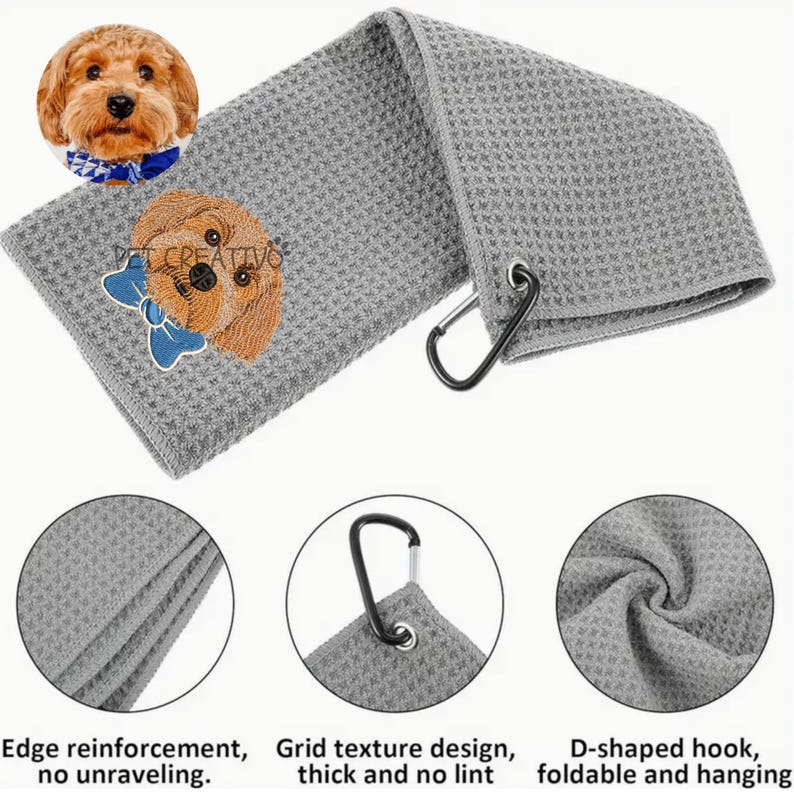 K&ouml;nnte beinhalten: Graues Golfhandtuch mit Waffelstruktur und einem gestickten Hund mit blauer Schleife. Mit D-f&ouml;rmigem Haken zum Aufh&auml;ngen und dem Text "PET CREATIVO". Das Handtuch hat eine Kantenverst&auml;rkung und ein Gittermuster.
