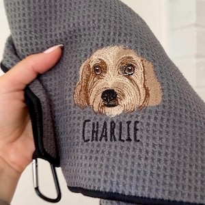 K&ouml;nnte beinhalten: Graues Waffelhandtuch mit schwarzem Rand und Metallclip. Das Handtuch zeigt ein gesticktes Hunde-Gesicht in Braun- und Beiget&ouml;nen, darunter der Name "CHARLIE" in Schwarz gestickt.
