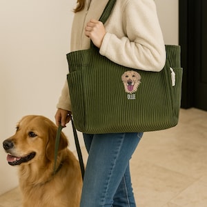 May include: Olive green corduroy tote bag with an embroidered golden retriever face and the name "Ollie" below. The bag has multiple pockets and is being held by a person. A golden retriever dog is on a leash next to the person.
