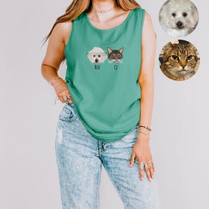 May include: Teal tank top with embroidered pet portraits of a dog and a cat, labeled "BLU" and "CJ". The words "PET CREATIVE" are above the portraits. The model is wearing light blue ripped jeans. Two pet portraits are in the background.
