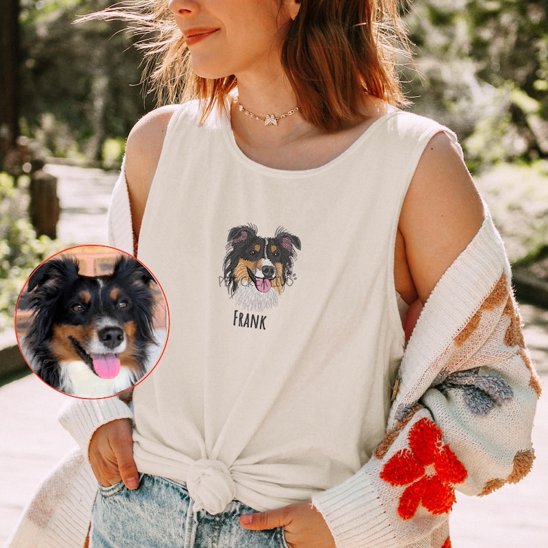 May include: Cream-colored tank top featuring a dog portrait with the name "FRANK" below it. The dog has black, brown, and white fur. The tank top is knotted at the waist.