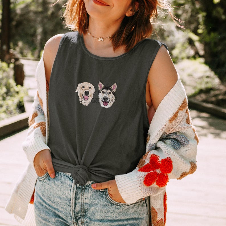 May include: Dark gray tank top featuring embroidered dog faces: a golden retriever and a husky. The top is knotted at the waist and paired with blue jeans. A white and patterned cardigan is worn over the top.