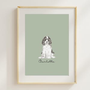 Op de afbeelding: Een ingelijste print van een zwart-witte hond die op een saliegroene achtergrond zit. De naam van de hond, Charlotte, staat in cursief onder de hond.