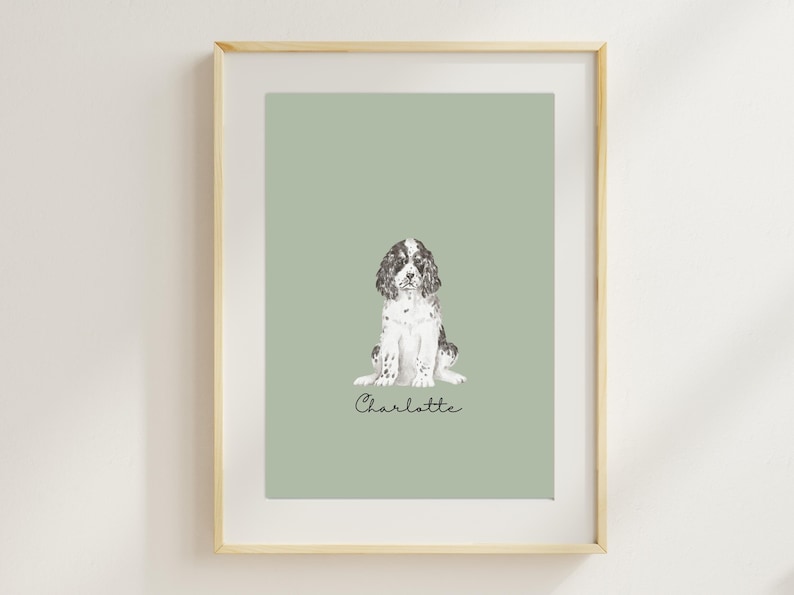 Op de afbeelding: Een ingelijste print van een zwart-witte hond die op een saliegroene achtergrond zit. De naam van de hond, Charlotte, staat in cursief onder de hond.